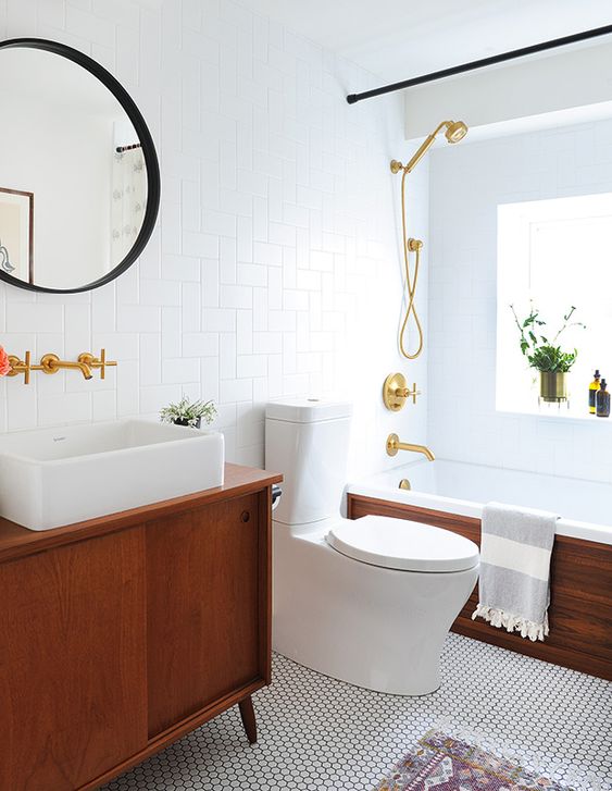 An elegant mid century modern bathroom with white penny and subway tiles, rich stained furniture, black and gold touches