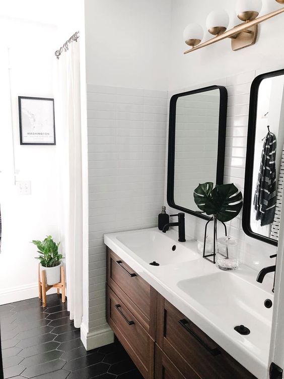 An elegant mid century modern bathroom with white tiles, a wooden vanity, black tiles on the floor and black fixtures