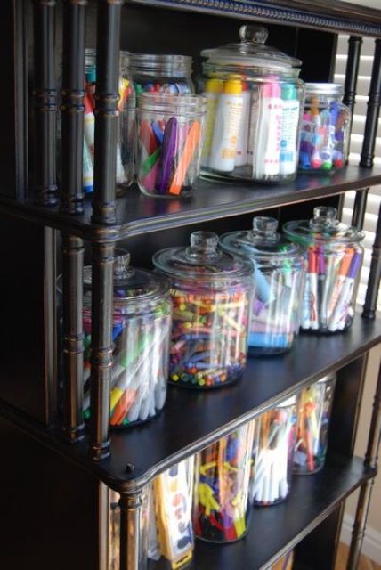 an open storage unit with large jars that are great to store crayons and markers