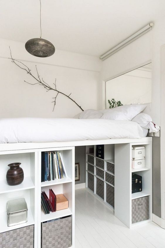 a creative tiny bedroom with a platform bed placed on storage units that create a whole wardrobe under it