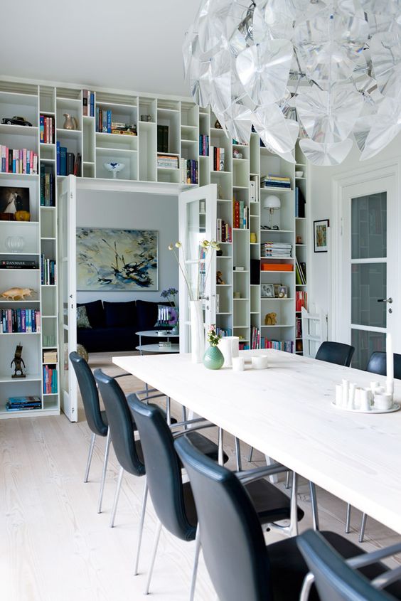 a dining room with a doorway wall taken by open shelves and displaying books, art and candleholders is a cool idea for saving space