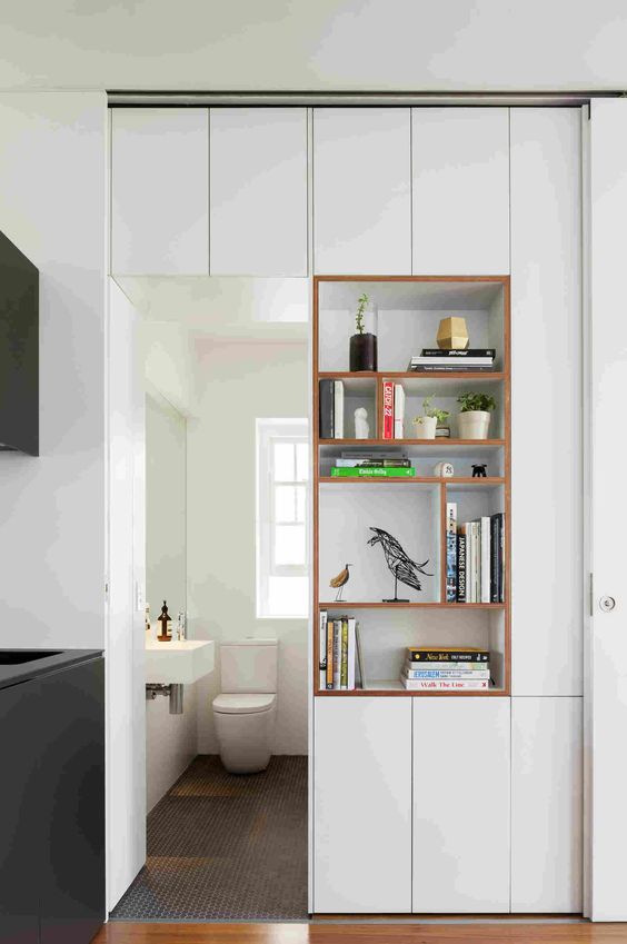 a doorway with open shelves and sleek cabinets right in the doorway is a cool idea to separate a small bathroom from another room