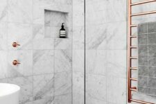a marble tile bathroom with a dark floor, a tub, a shower and copper hardware for a chic and bold look