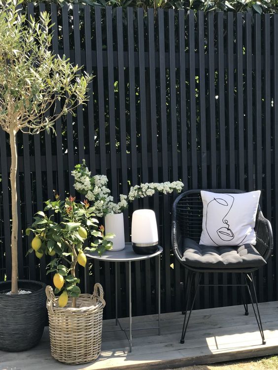 a pretty outdoor Scandinavian space with a grey metal side table, a black wicker chair with pillows, potted plants and a lemon tree