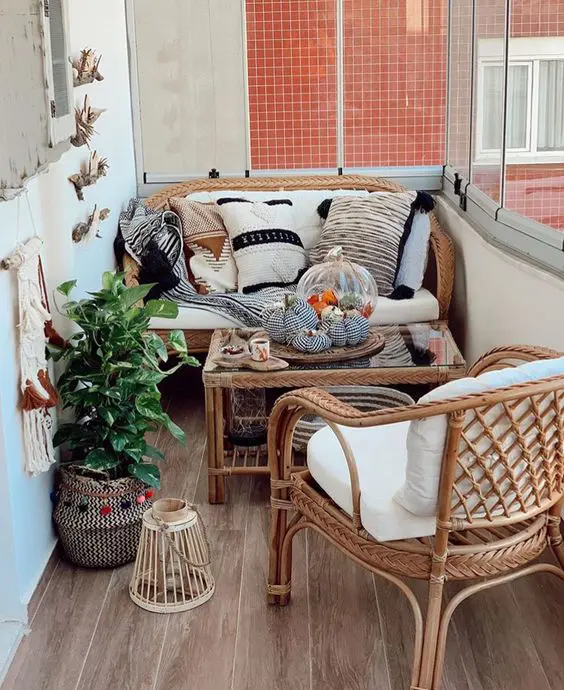 a pretty small balcony done with a wicker loveseat, a chair and a coffee table with a glass tabletop, a potted plant and some candle lanterns