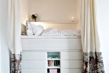 a tall bed built of several layers of drawers and open storage ocmpartments is a cozy and functional unit