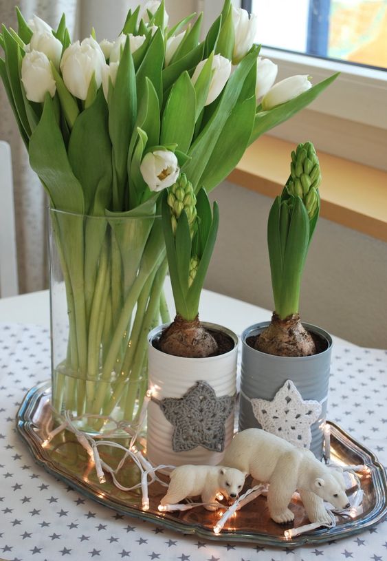 a tray with lights, bears, bulbs in tin cans with crochet stars and white tulips in a vase for a Nordic feel