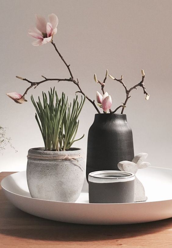 elegant Nordic spring decor with a bowl with a concrete planter with greenery, a black vase with cherry blossom, a candle and a bunny