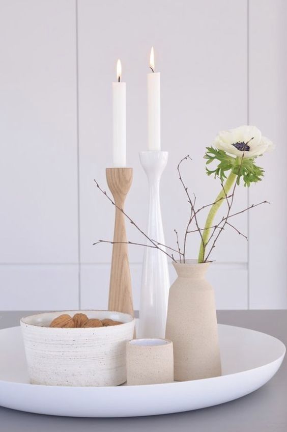 minimal Nordic decor with a tray with a bowl with nuts, candles in simple candlesticks and a vase with a bloom and branches