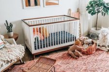 a boho nursery with a bright red ru, boho hangings, mid-century modern artworks and fluffy touches