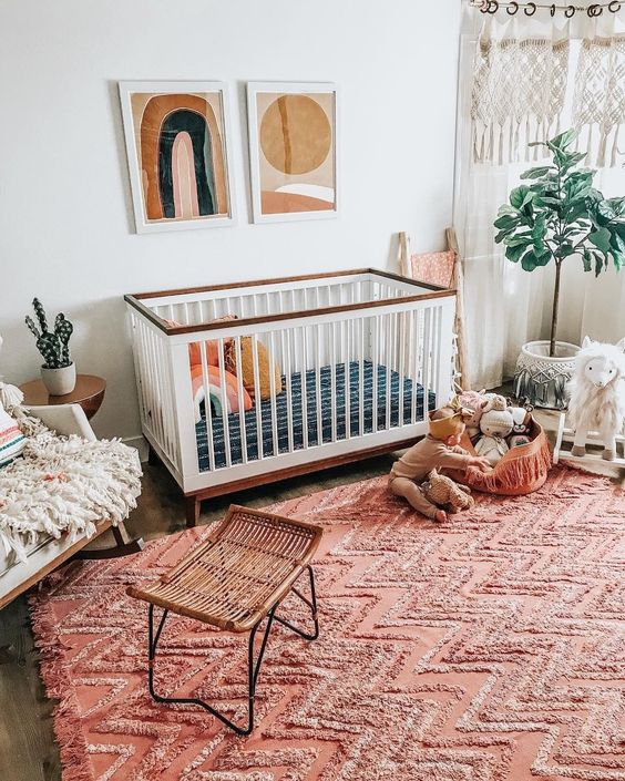 A boho nursery with a bright red ru, boho hangings, mid century modern artworks and fluffy touches