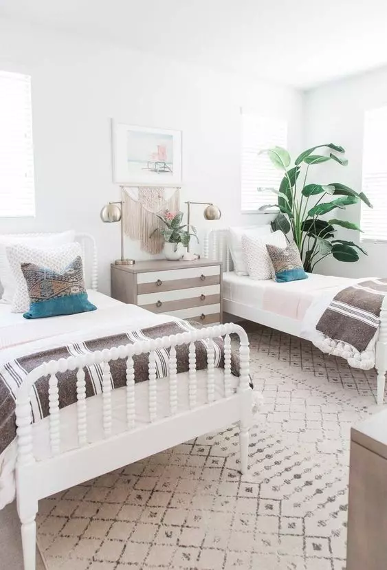 a boho shared kids' bedroom with white beds, stained dressers, brass table lamps and potted plants plus boho decor