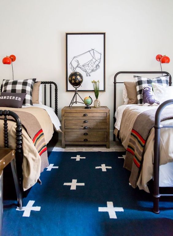 a bold shared teen boy bedroom with black beds, layered rugs, bright bedding, a gallery wall and red sconces