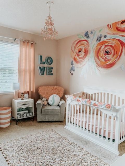 a bright and cool girl nursery with painted flowers, white and grey furniture, peachy pink bedding and a lovely coral chandelier