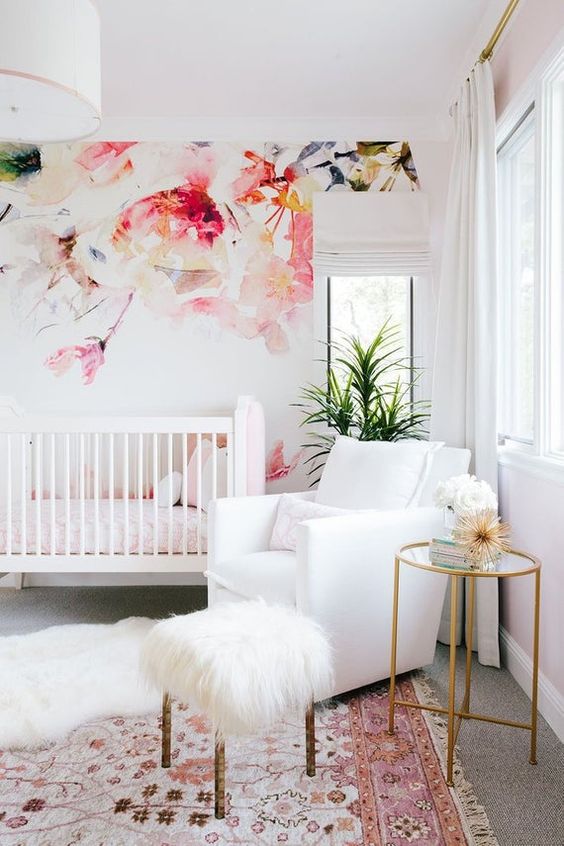 a bright girlish nursery with a bold floral accent wall, white furniture, a bold printed rug, a mini side table and potted plants