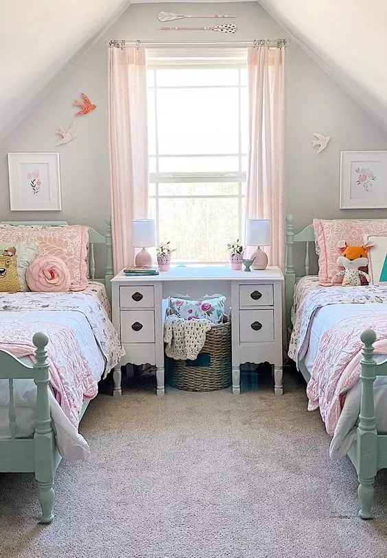 a chic attic kids' bedroom with mint vintage beds, pastel bedding, a white carved desk and a basket, blush curtains and some pretty decor on the walls