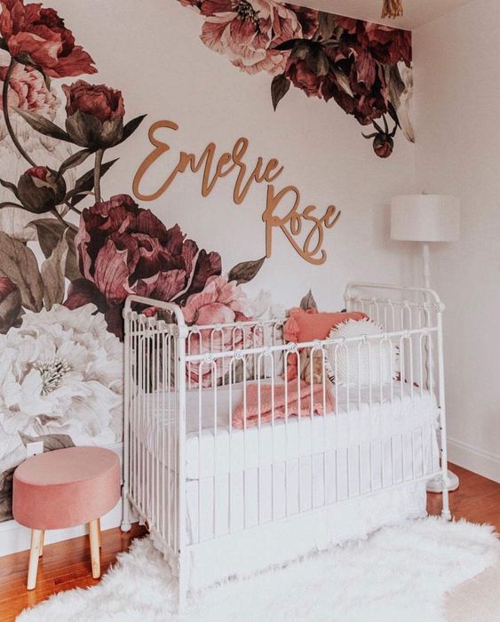 a chic girl nursery with a bold floral mural on the wall, white furniture, a pink stool and white and coral bedding