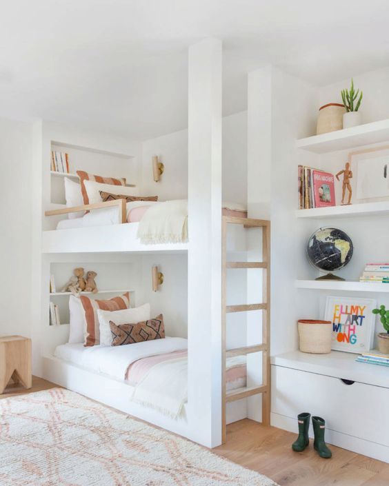 A chic neutral kids' bedroom with a bunk bed with a wooden ladder, built in shelves and a drawer, cool printed textiles