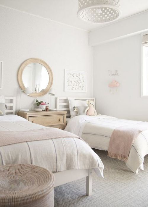 a chic neutral shared bedroom with white beds and a stained dresser, neutral and pink bedding, a mirror in a wooden frame, a white pendant lamp and a basket for storage