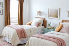 a chic shared girls’ bedroom with a bright printed rug, cane headboard beds with pastel and mustard bedding, mustard curtains and a mint blue nightstand
