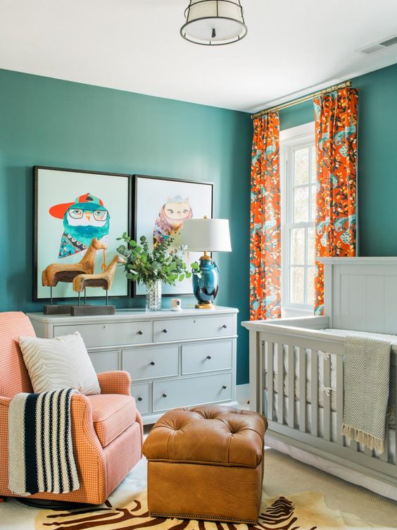 a colorful gender neutral nursery done in turquoise and orange, with white furniture, an orange chair and a leather ottoman plus bold artworks
