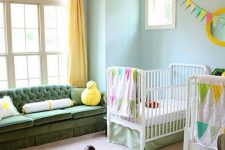 a colorful shared nursery with blue walls, white and green furniture, touches of bright yellow and bright printed textiles