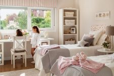 a cool neutral shared girls’ bedroom with vintage furniture, a desk by the window and chairs, pink and grey textiles and lamps