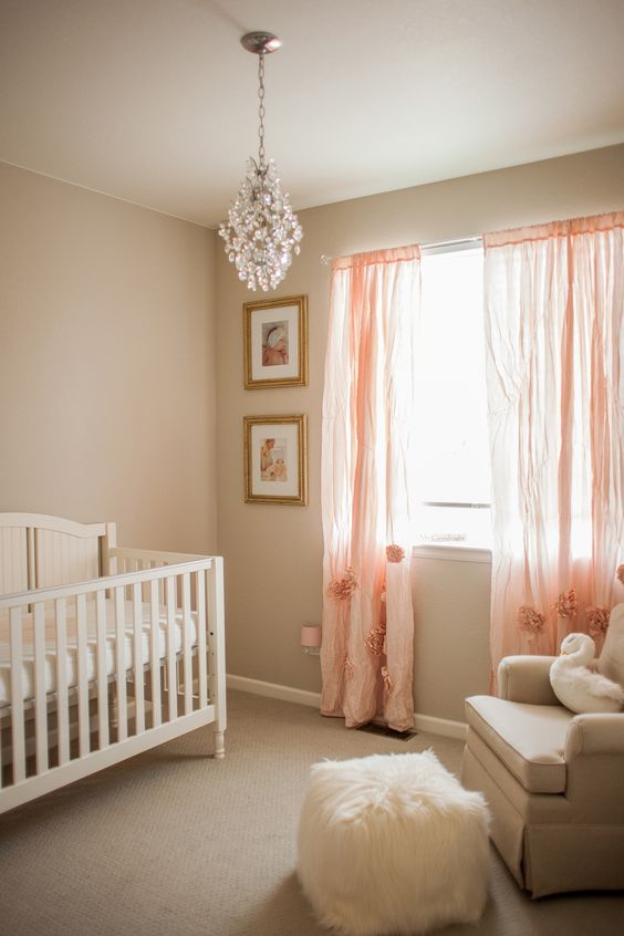 a cute girl nursery done in warm neutrals, with pink curtains with fluffs, a crystal chandelier and neutral bedding
