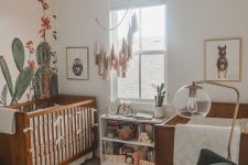 a desert themed nursery with stained cribs, a hunter green chair, a tassel hanging and a cactus accent wall