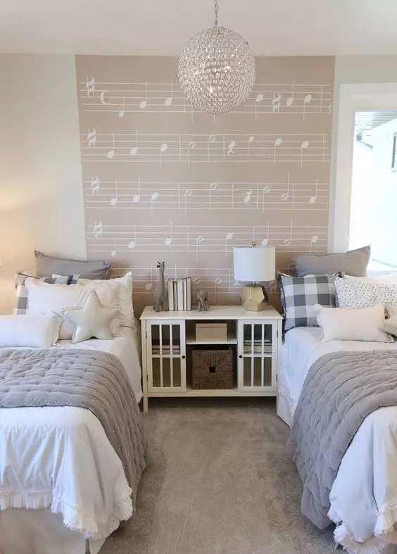 a dreamy neutral shared girls' bedroom with white beds and a storage unit, grey and white bedding, a music accent wall, a crystal pendant lamp
