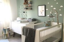 a gender neutral nursery with a green wall, minimal and sleek furniture, a green pendant lamp and some art and accessories