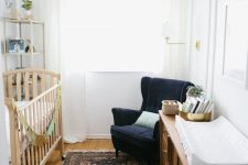 a gender neutral nursery with retro wooden furniture, a navy chair, a boho rug and shelves