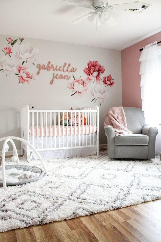 a grey and mauve nursery with a floral mural, a mauve wall, white and grey furniture and pink textiles
