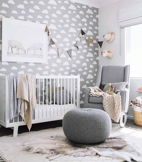 a grey gender neutral nursery with a cloud accent wall, chic white and grey furniture and garlands and faux taxidermy