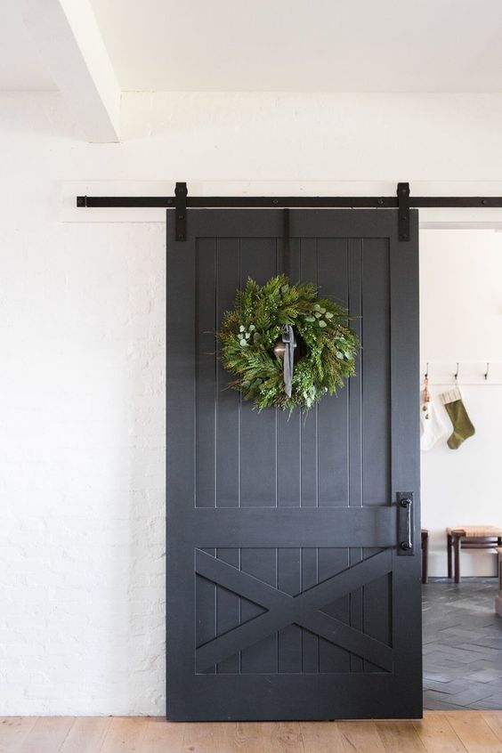a grey sliding barn door with handles with a large greenery wreath brings a cheer holiday feel
