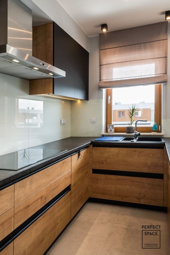 a light-stained and black modern kitchen with black countertops and a neutral glas sbacksplash plsu stainless steel appliances