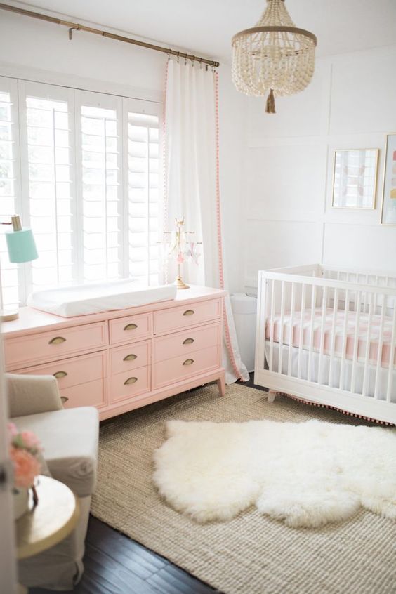 a lively girl nursery in white, with white and pink furniture, layered rugs, pink and white bedding and a beaded chandelier