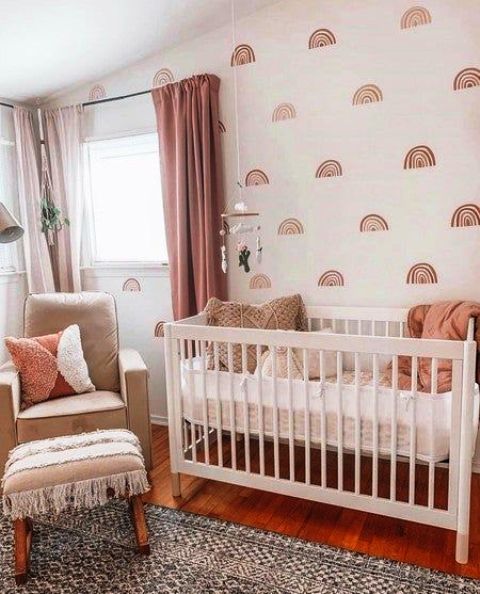 a lovely boho girl’s nursery with a printed wall, simple neutral furniture, pink curtans and pink bedding