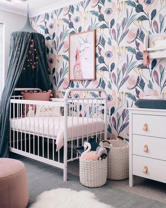 a lovely girl nursery with a beautiful floral mural wall, white furniture, a teal canopy and cushions, pink ottomans and baskets