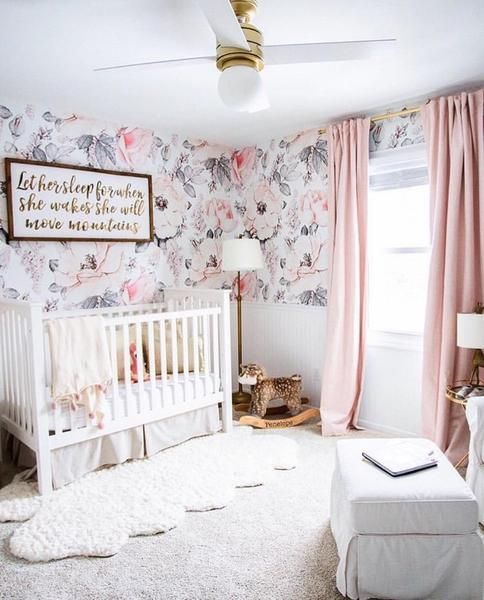 a lovely nursery with floral walls, white furniture, pink curtains, pretty modern lamps and layered rugs is cozy