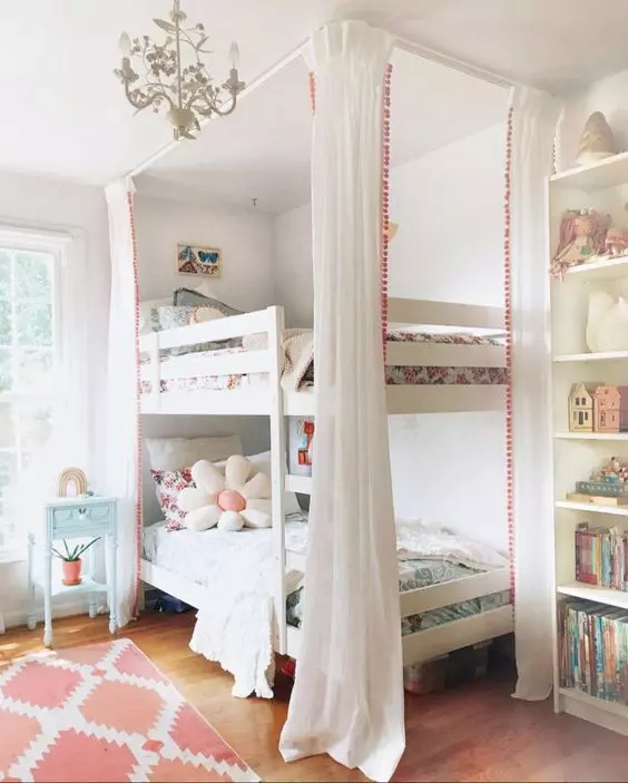 A lovely shared girls' bedroom with a built in bookcase and a bunk bed, pastel and white bedding, a coral rug and a blue nightstand