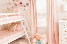 a lovely shared girls’ bedroom with pink floral walls, a bunk bed, a white nightstand, pink textiles and some cute toys