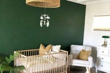 a mid-century modern boho nursery with a green accent wall, white and light-colored furniture, a printed rug and a woven lamp