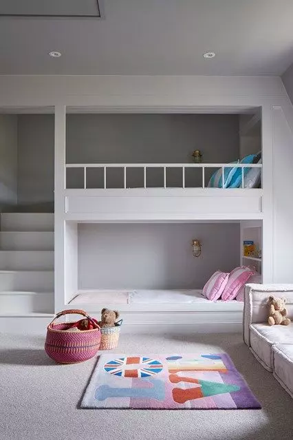 A minimalist shared girls' bedroom with bunk beds and built in shelves, a sofa by the window and bright printed textiles