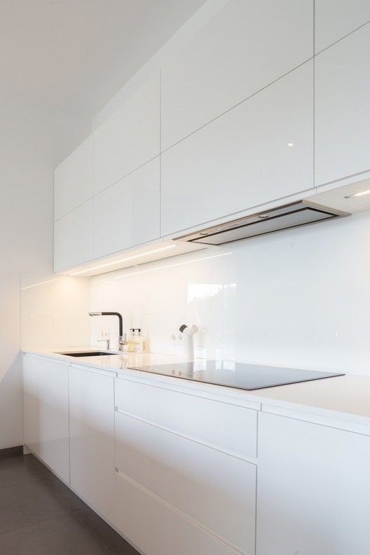 a minimalist white kitchen with sleek cabinets, stone countertops and a glass backsplash plus stainless steel appliances