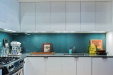 a modern white kitchen with black countertops, a teal glass backsplash and additional lights is a gorgeous idea with much contrast