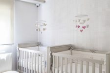 a neutral and peaceful shared nursery with off-white furniture, a cloud lamp and cloud mobiles is welcoming