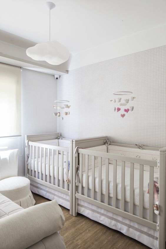 A neutral and peaceful shared nursery with off white furniture, a cloud lamp and cloud mobiles is welcoming