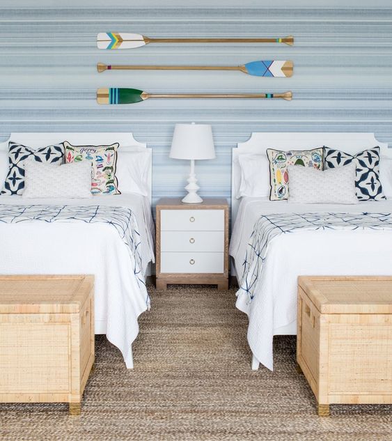 a neutral beach shared bedroom with two beds, wicker chests for storage and oars on the wall