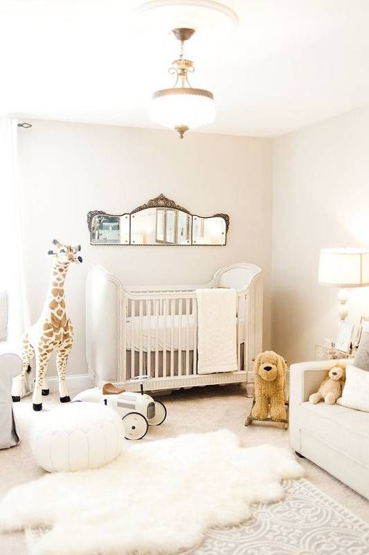 a neutral nursery with a refined crib, white furniture, a vintage mirror and layered rugs plus chic toys